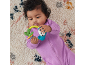 Baby in a purple romper playing with a colorful rattle on a textured rug.