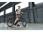 Man in grey sportswear and helmet, standing next to a black electric bicycle.