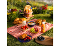 Picnic blanket filled with croissants, fruits, and sunscreens on green grass.