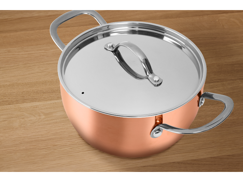 Copper pot with a metal lid and handles on a wooden table.