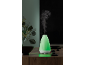 Green essential oil diffuser with steam, surrounded by plants and stones.