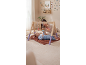 Baby playing with a wooden activity gym with hanging toys, with mom in the background.