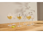 Six wine glasses, three filled with white wine, on a wooden table with grapes.