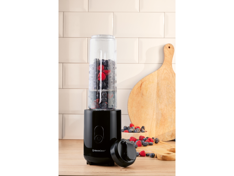 Black personal blender with a jug full of berries and water, on a wooden countertop.
