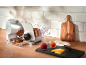Bread slicer with sliced bread, jam, and cheese on a wooden counter.