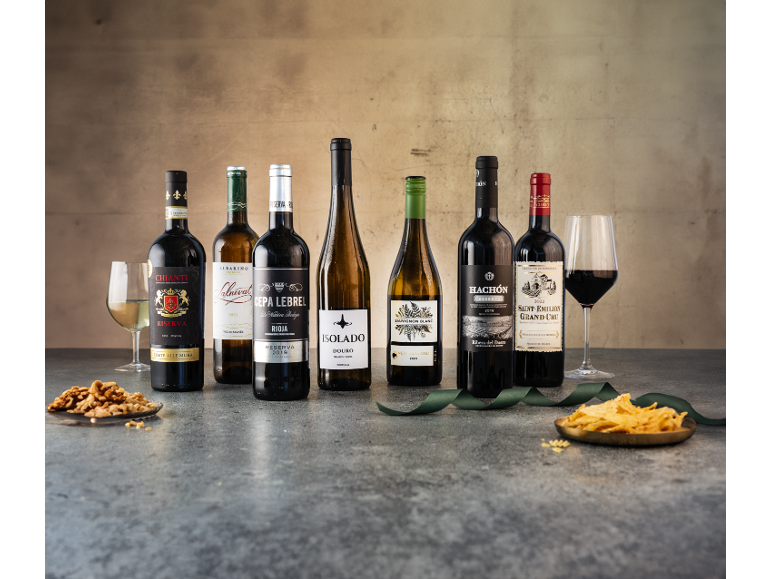 Seven wine bottles, including red, white, and rosé, with glasses and snacks, on a textured background.
