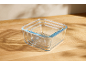 Three nested square glass food storage containers on a wooden surface.