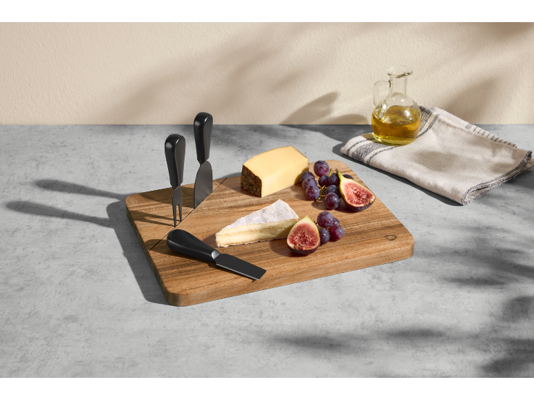 Cheese board with cheeses, grapes, and figs, accompanied by cheese knives and an oil bottle.