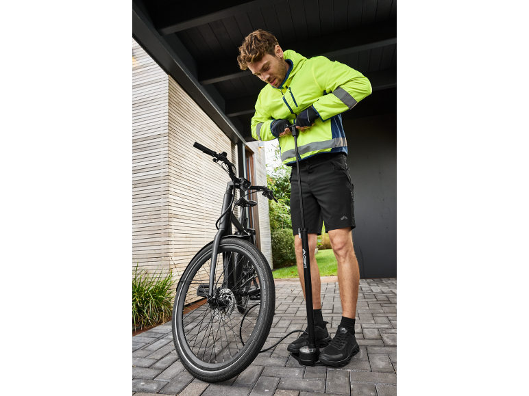Man in cycling jacket and shorts inflates bike tire with a floor pump.