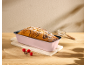 Pink loaf pan with a cake dusted with powdered sugar on a wooden table.