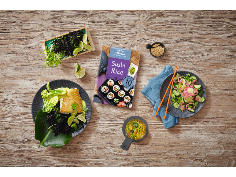 Sushi rice, fish with black rice, and cucumber salad on wood.