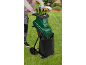 Man using a garden shredder, grinding leaves into a black bag in a garden.