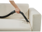 Hand vacuuming dirt from a light-colored sofa with an attachment.