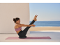 Woman doing Pilates on a yoga mat with a balance cushion, overlooking the sea.