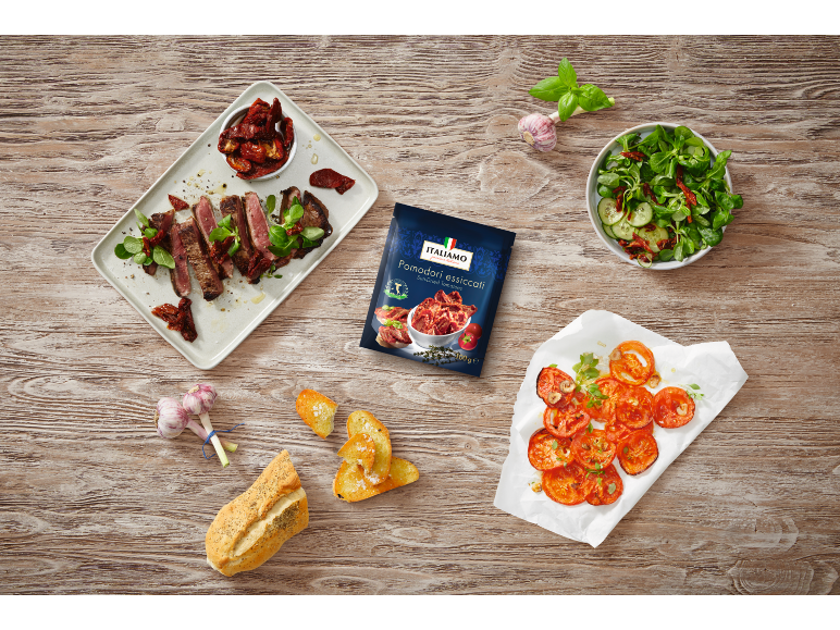 Sun-dried tomatoes in a pouch, served with seared steak, salad, and bread on a wooden table.