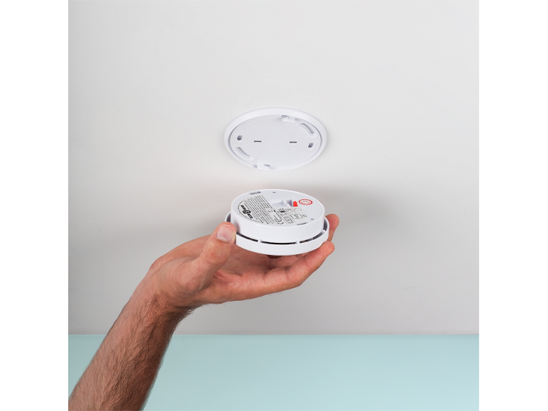 Hand holding a smoke detector, ready for ceiling installation.