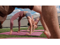 Women in sports tops and leggings doing yoga on pink mats on grass.