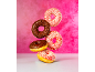 Five chocolate and strawberry donuts with sprinkles, some levitating against a pink background.