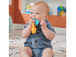 Smiling baby in a denim romper playing with a colorful rattle on a rug.