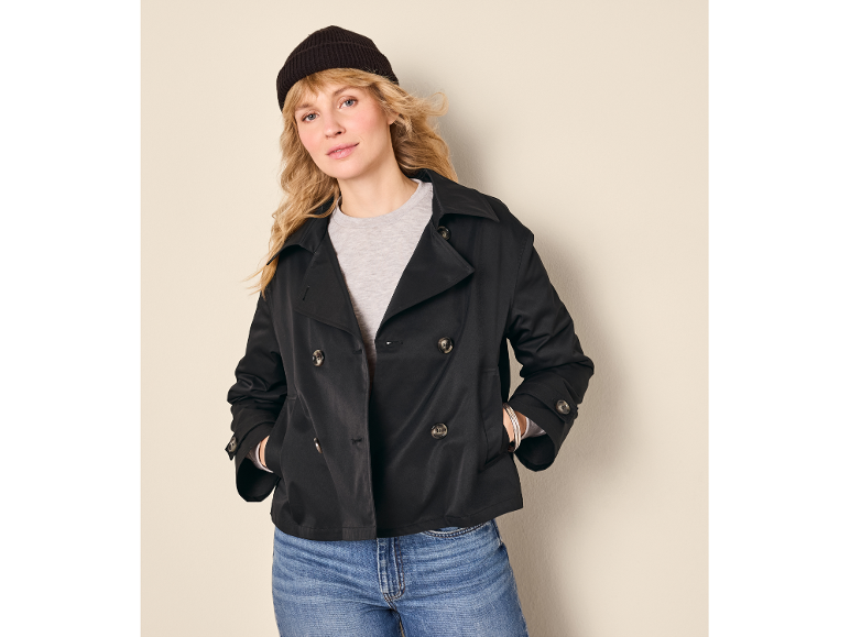 Woman in black pea coat, grey t-shirt, blue jeans, and black beanie.