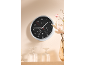 Wall clock with thermometer and hygrometer on a light beige wall, with a vase of flowers.