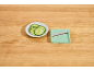 Sliced cucumbers on a plate next to a mint green mandoline on a wooden table.