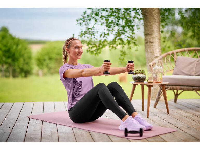 Woman in purple t-shirt and black leggings exercising with dumbbells on a yoga mat.