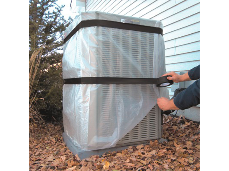 A person covers an outdoor air conditioning unit with a protective cover and secures it with tape.