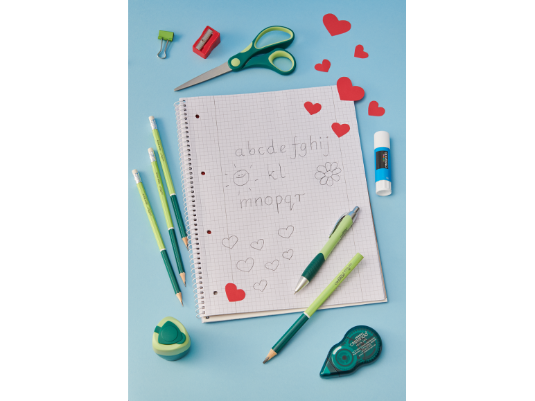 Green and red school supplies with a notebook featuring a drawn alphabet and hearts.