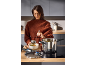 Woman ladling soup from a stainless steel pot into a bowl in the kitchen.