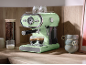 Light green espresso coffee machine with two cups on a wooden counter.