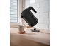 Black kettle pouring hot water into a mug on a wooden countertop.
