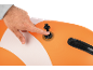A hand pressing the inflation valve of an orange and white inflatable paddleboard.