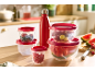 Red food containers and water bottle with fruit on a kitchen table.