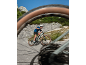 Man cycling uphill on an electric mountain bike, seen through a blurred bicycle wheel.