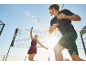Two people playing badminton outdoors, with a net, rackets, and shuttlecock visible.