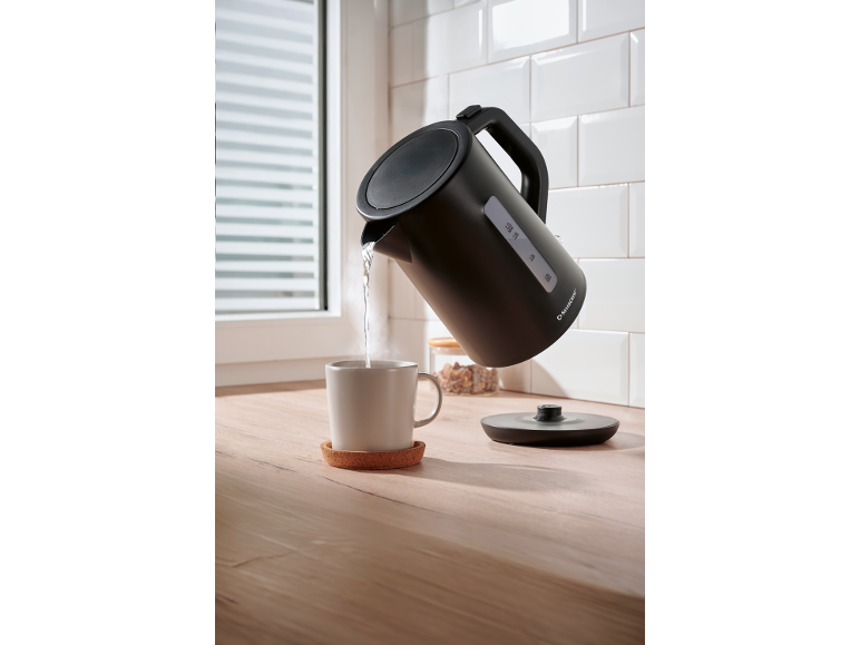 Black kettle pouring hot water into a mug on a wooden countertop.