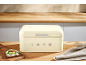 Cream-colored bread bin with the number 1973, on a wooden table with bread.