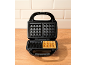 Open waffle maker with a baked waffle on a wooden table.