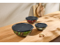 Three glass bowls with black lids, filled with salad, strawberries, and nuts, on a wooden countertop.