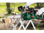 Green chainsaw cutting a wooden log on a sawhorse in an outdoor setting.