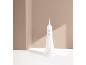 White dental irrigator with a charging base on a white surface against a beige background.