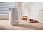 White electric kettle on a wooden countertop with cookies and tiles in the background.