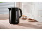 Matte black electric kettle on a light wooden countertop with white tiles.