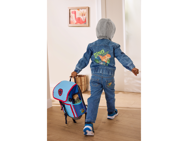 Boy in a dinosaur denim jacket and jeans, carrying a blue backpack.