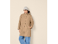 Woman in a beige parka, grey beanie, and jeans, hand in pocket.