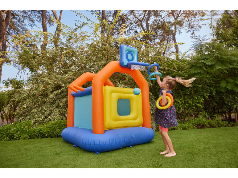 Girl playing with a colorful inflatable bouncy castle with a basketball hoop and rings in the garden.