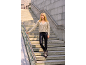 Woman in a beige cardigan and black faux leather leggings on concrete stairs.