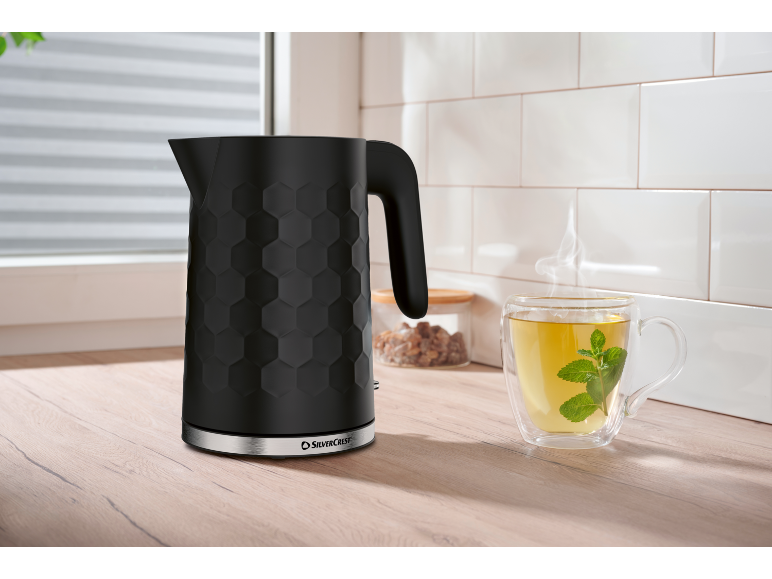 Black hexagonal pattern kettle and steaming mint tea cup on a wooden countertop.