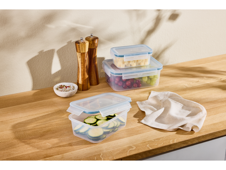 Plastic food containers, wooden salt and pepper grinders, and a kitchen towel on a wooden table.